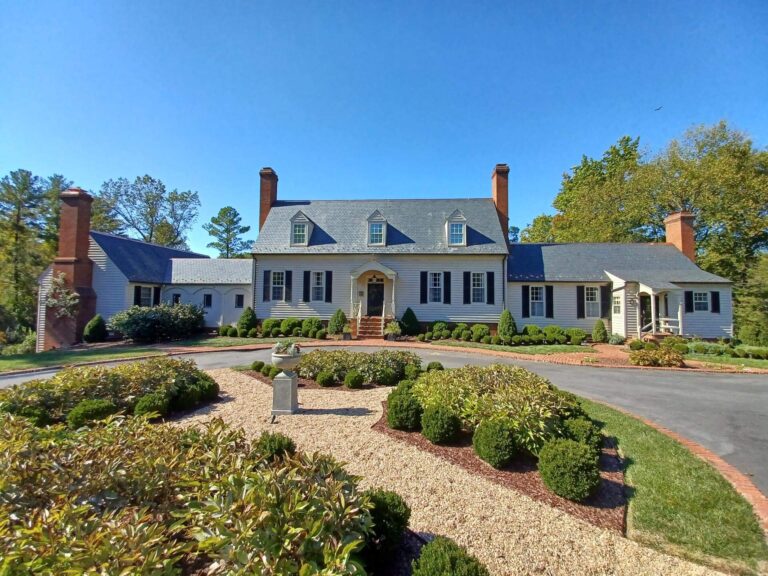 Large white house with dark roof, red brick chimneys, and landscaped front yard on a sunny day