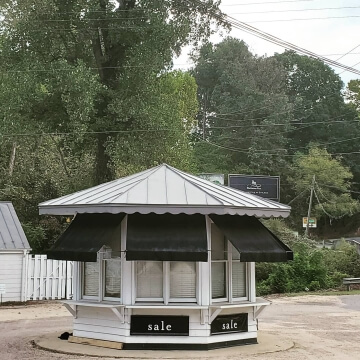 Small white kiosk with black awnings and sale signs