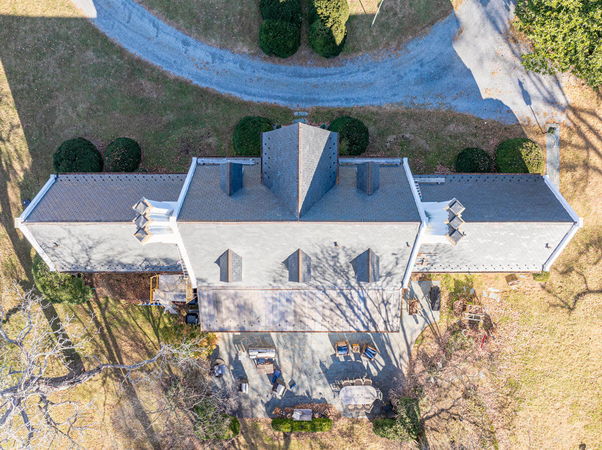 Aerial view of a house with a gray roof, surrounded by a driveway and yard